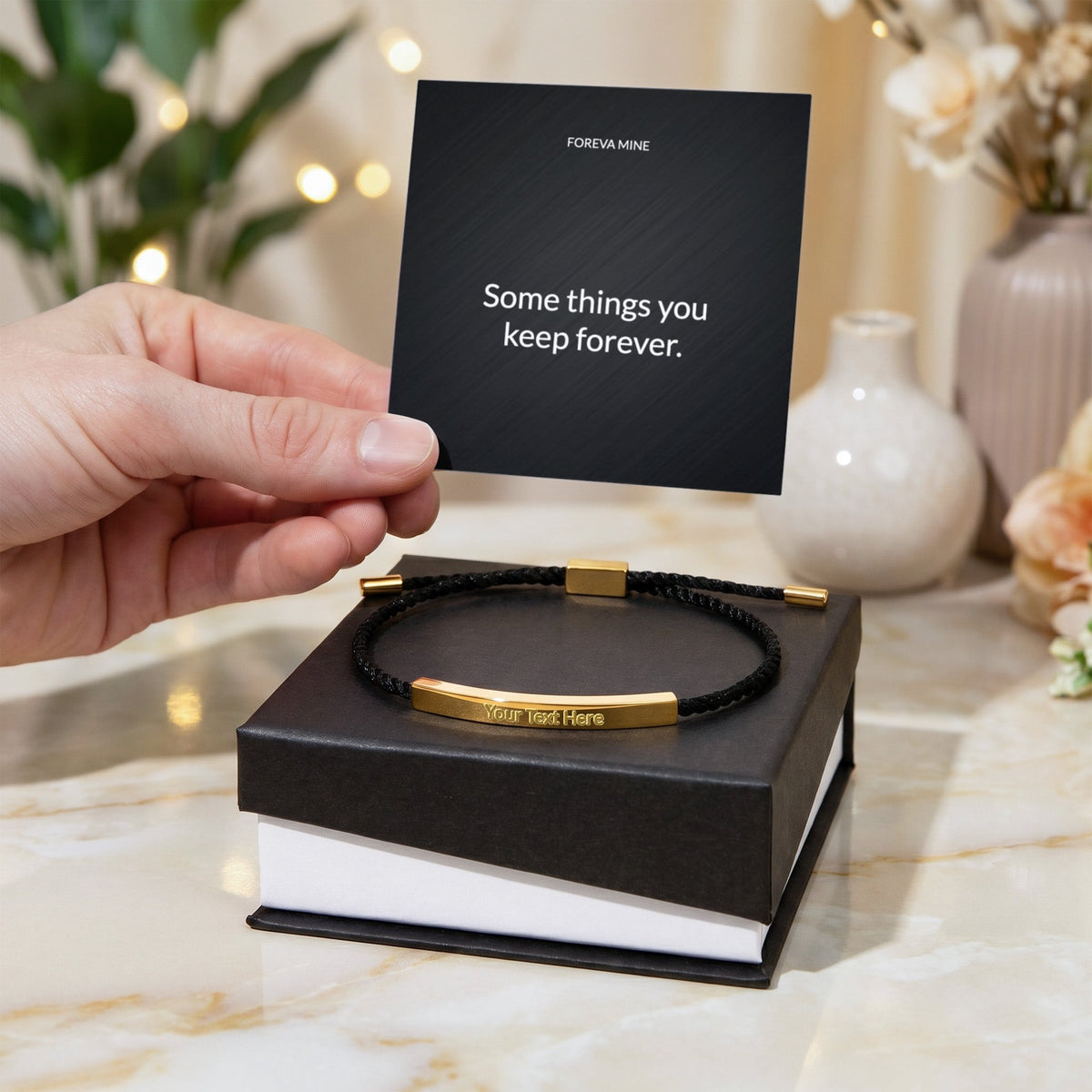A hand holding the Foreva Mine message card above a gift box with the gold engraved cord bracelet resting on it